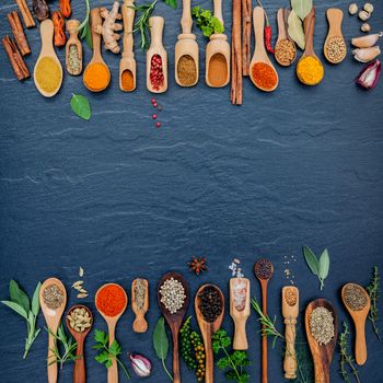 Various of spices and herbs in wooden spoons. Flat lay of spices ingredients chilli ,pepper corn, garlic, thyme, oregano, cinnamon, star anise, nutmeg, mace, sage and parsley on the black stone.