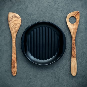 Wooden cooking utensils wooden spoons, spatula and black plate on dark background. Blank dish and copy space for menu design.