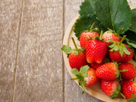 Strawberries from the garden that is placed on a wooden tray.