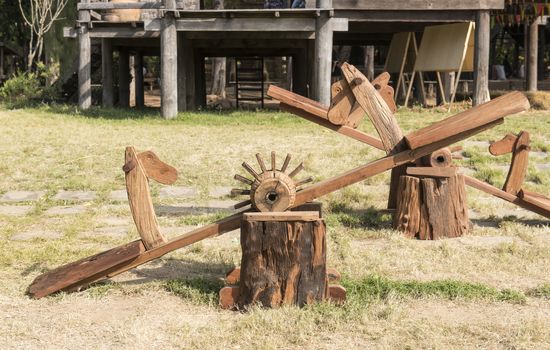 Empty wooden seesaw in garden with old houses in the countryside.