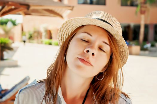 Pensive young woman with closed eyes in a straw hat, close-up portrait.