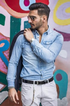 Attractive young man sitting against colorful graffiti wall, looking to a side