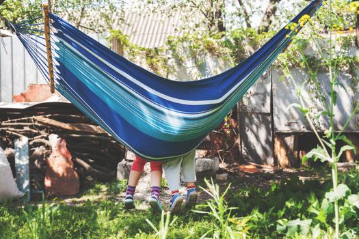 Children's feet in blue hammock on a background of nature greenery.