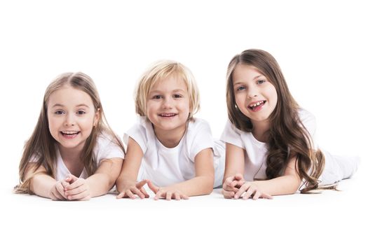 Happy smiling three children in white clothes laying on floor isolated on white background