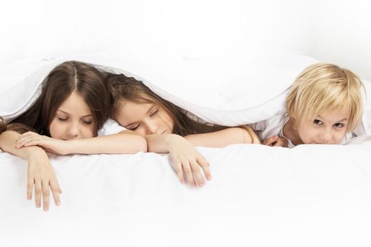 Three beautiful children sleeping in bed under one white blanket