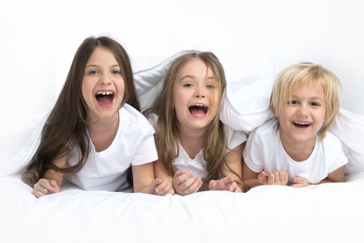 Three happy smiling children waking up in bed under one blanket