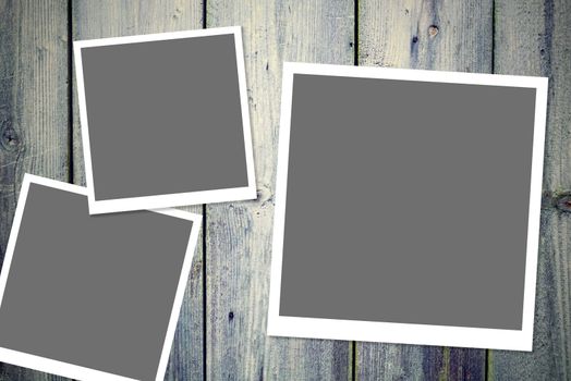 Three instant vintage white photo frames with blank gray space placed on the wooden desk.