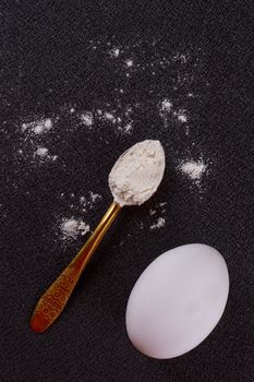 Gold-plated spoon, flour, egg on a black background