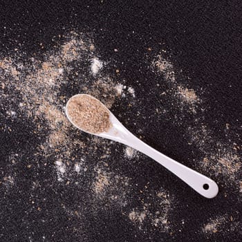 White whole-wheat flour and a spoon on a black background
