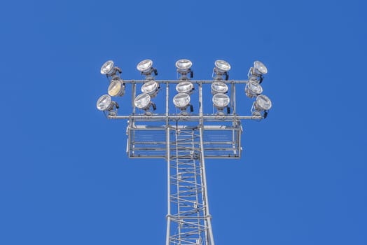 Stadium lights switched off on a metallic tower against a blue sky.