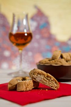 Closeup of Italian cantucci biscuits over a red napkin and a glass of vin santo wine on background