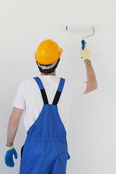 Worker in overalls uniform and hardhat painting the wall with paint roller