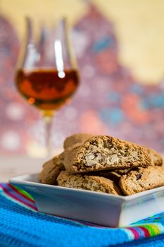 Closeup of Italian cantucci biscuits on a blue napkin and a glass of vin santo wine on background