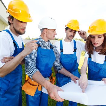 Team of workers with blueprint at construction site