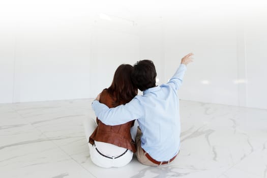 Young couple sitting on the floor of new empty house pointing up into the air