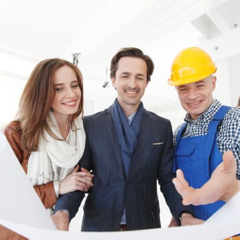 Worker shows house design plans to a young couple at construction site