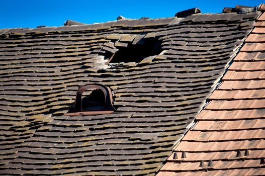 Old damaged tiled roof with broken tiles and a hole on the roof