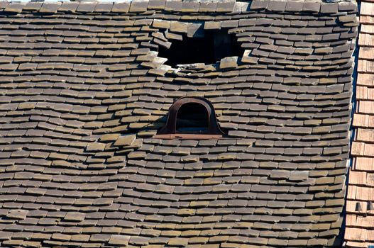 Old damaged tiled roof with broken tiles and a hole on the roof