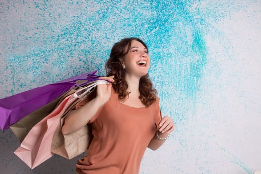 Happy smiling woman at shopping holding colourful paper bags near blue wall