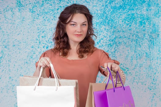 Happy smiling woman in orange blouse holding colourful shopping paper bags