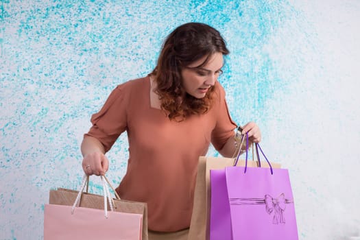 Worried woman in orange blouse holding colourful shopping paper bags in her hads