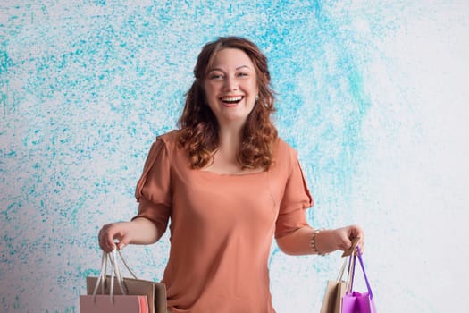 Happy smiling woman in orange blouse holding colourful shopping paper bags