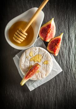 A wheel of melted brie covered in sliced figs and honey  on a stone plate.