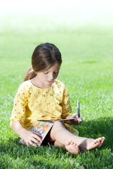 portrait of little girl studying on the grass in summer environment