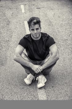 Attractive smiling man sitting in the middle of city street looking at camera