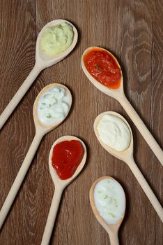 different types of sauces in spoons on wooden table