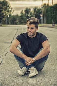 Attractive smiling man sitting in the middle of city street looking away