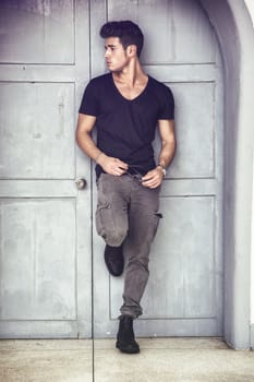 Handsome young man outdoors in front of old house's wood entrance door, looking away to a side