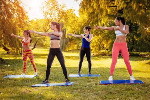 Four beautiful female friends doing stretching exercise in the park. 