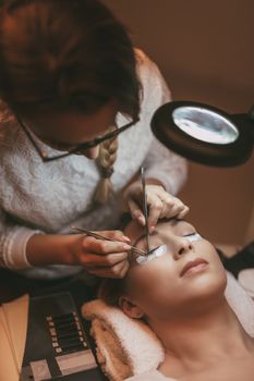 Beautician applying extended eyelashes to model at the beauty salon.