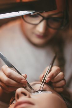 Beautician applying extended eyelashes to model at the beauty salon.