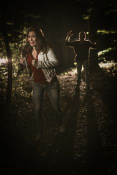 Young scared woman running through the forest at night in white dress and running away from man.