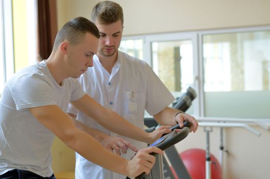 Young man on exercise bicycle in physiotherapy gym center 