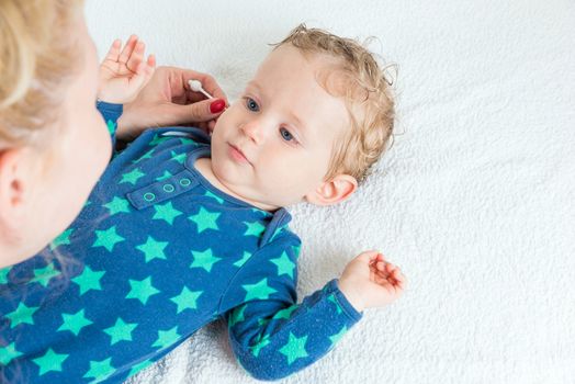 Mother hand cleaning baby ear with cotton swab,infant lying with wet hair and blue eyes,copy space,horizontal photo.