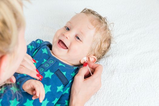 Mother hand cleaning baby ear with cotton swab,infant lying with wet hair and blue eyes and smiling,copy space,horizontal photo.