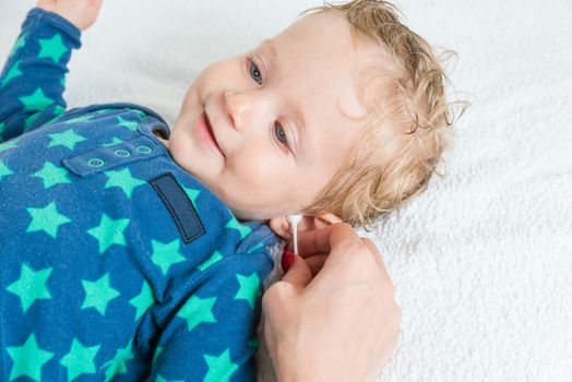 Mother hand cleaning baby ear with cotton swab,infant lying with wet hair and blue eyes and smiling,copy space,horizontal photo.