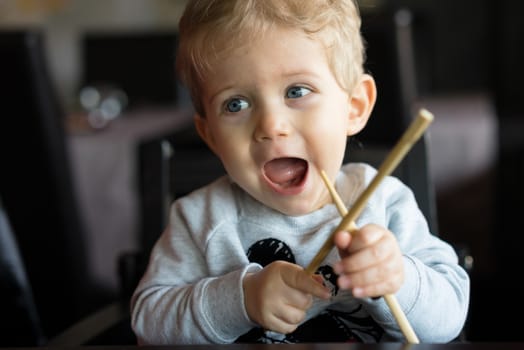 Baby boy sitting in high chair and plays with chopsticks at chinese restaurant.