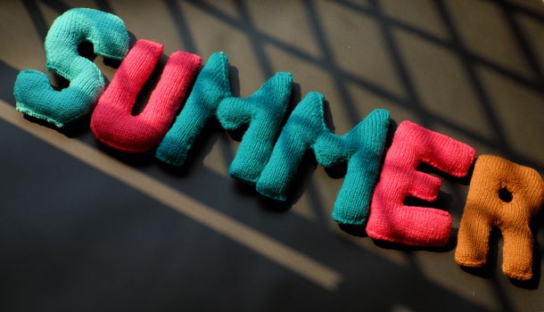 Summer background from knitted alphabet on black background, summertime letter knit from colorful yarn, wonderful handmade product