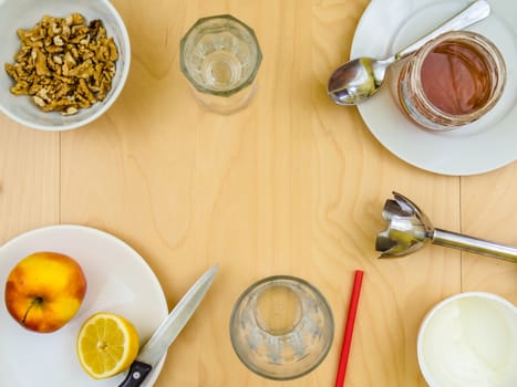 Ingredients for a healthy and nutritious snack or smoothie with utensils and copy space, apple lemon fruit, cottage cheese, honey , shelled nuts walnuts, on plates from top view, arranged on wooden table in soft colours