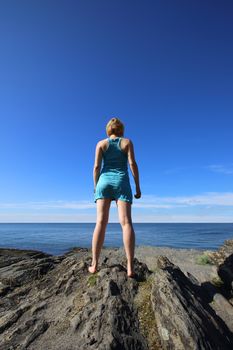 Woman standing on rock , looking at ocean, vacation concept