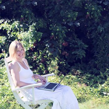 Woman working on a laptop outdoors in summer garden