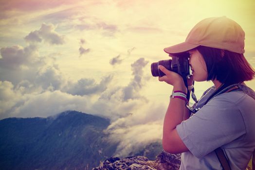 Vintage style hiker asian teens girl with digital camera taking photo beautiful landscape natural of sierra and sky during sunset on mountain at Phu Chi Fa Forest Park, Chiang Rai, Thailand