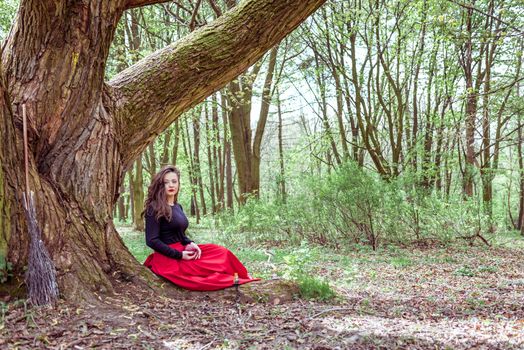 mystical witch woman sitting under a old tree in the forest