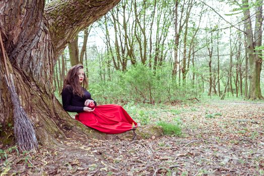 mystical witch woman sitting under a old tree in the summer park