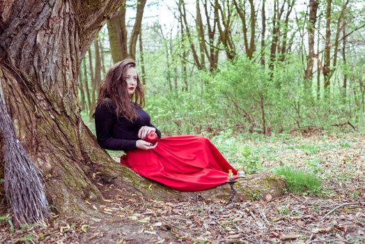 mystical witch woman sitting under a old tree in the forest