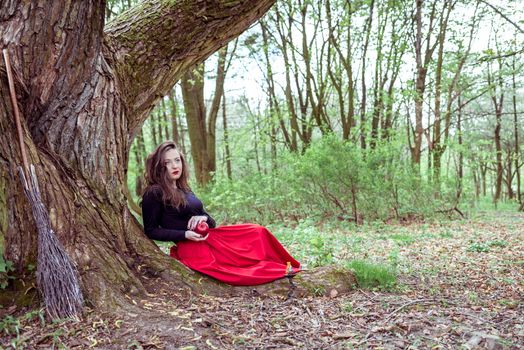 mystical witch woman sitting under a old tree in the summer park